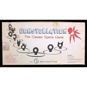 Op de afbeelding: Een vintage bordspeldoos met een rood en wit zonontwerp. Het spel heet "Constellation: The Classic Space Game". De doos is wit met zwarte tekst en een zwart-witte illustratie van het spelbord.