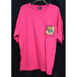 May include: A pink t-shirt with a colorful graphic on the pocket. The graphic features a cartoon character with a blue background.