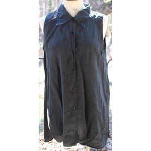 Könnte beinhalten: Ein schwarzes, ärmelloses Hemd mit Knöpfen und Kragen. Das Hemd hat eine lockere Passform und eine etwas längere Länge.