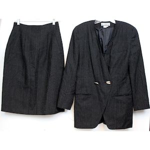 May include: A black skirt and blazer suit with a white polka dot pattern. The blazer has a single button closure and a silver accent on the lapel.