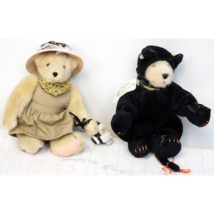 Può includere: Due orsacchiotti di peluche, uno vestito da esploratore con un cappello e una sciarpa a stampa leopardata, l'altro vestito da gatto nero con una maschera nera e una coda.