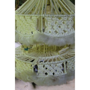 May include: A white macrame lampshade with a fluffy white trim. The lampshade is made of a thick rope and has a circular shape.