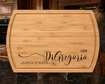 May include: A rectangular bamboo cutting board with a juice groove along the perimeter. The board is engraved with the text DiGregorio, the names JAMES and NATALIE separated by a heart symbol, and the year 2026 in a black script and sans-serif font.