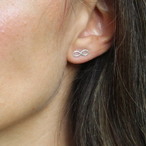 May include: A close-up of a person's face and neck, with a silver infinity symbol stud earring in the right ear. A silver necklace is visible. The person is wearing a light green top.