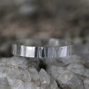 May include: A silver ring with a hammered texture. The ring is sitting on a bed of white crystals.