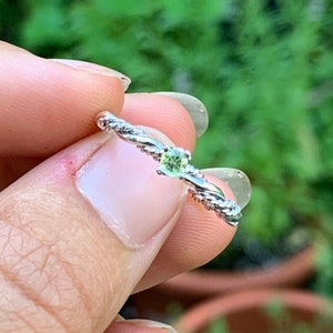 Puede incluir: Un anillo de plata con una banda trenzada y una pequeña piedra preciosa verde.