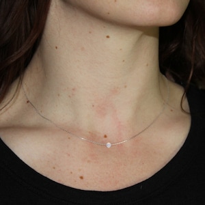 May include: A delicate silver chain necklace with a single small, round, clear gemstone pendant.