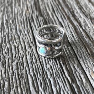 May include: Silver ear cuff featuring a white opal gemstone. The cuff is made of multiple bands of metal that wrap around the ear.