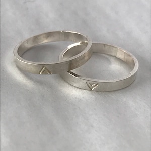 May include: Two silver rings with a triangle design engraved on each. The rings are stacked on top of each other.