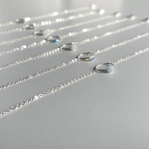 May include: A set of silver chain bracelets, each featuring a small, round gemstone charm. The gemstones are in a variety of colours, including blue, purple, and white.