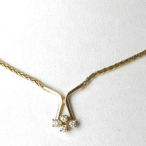 May include: A gold-toned necklace with a delicate chain and a pendant featuring four small, clear gemstones. The pendant is set in a stylized, open-work design. The necklace is displayed against a white background.