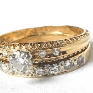 May include: A gold ring with a central diamond and smaller diamonds set around the band. The ring has a detailed, textured design and is set against a white background. The ring is a piece of jewelry.