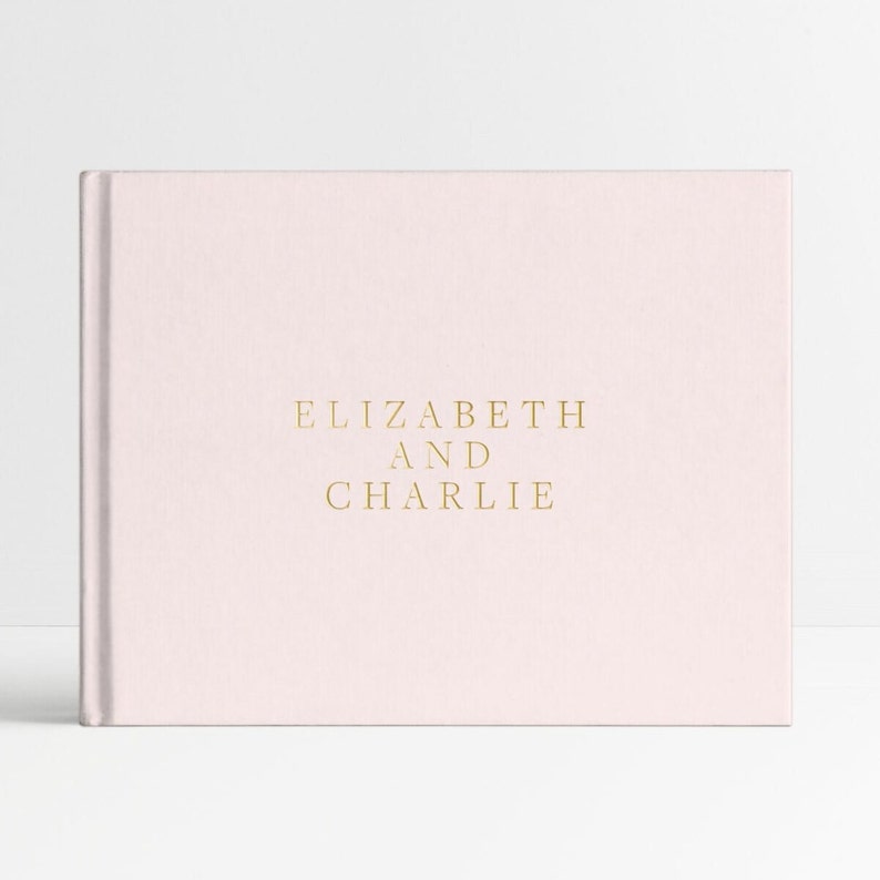 May include: A pale pink linen-covered photo album with the text "ELIZABETH AND CHARLIE" in gold lettering.