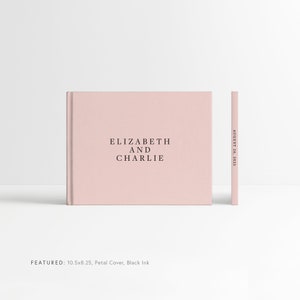 May include: A blush pink hardcover photo album with the text "ELIZABETH AND CHARLIE" and the date "AUGUST 26, 2023" printed on the spine. The album is 10.5 inches by 8.25 inches and features a petal cover with black ink.