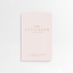 May include: A pink booklet with gold lettering that reads "THE OFFICIANT STEPHEN FRAZZA ELIZABETH AND CHARLIE AUGUST 26, 2023"