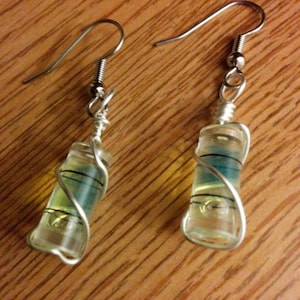May include: A pair of silver earrings with clear glass teardrop-shaped charms wrapped in silver wire. The charms have a blue and green liquid inside.