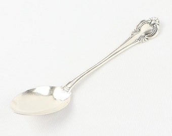 May include: A silver teaspoon with an ornate handle. The spoon has a rounded bowl and a long, slender handle.