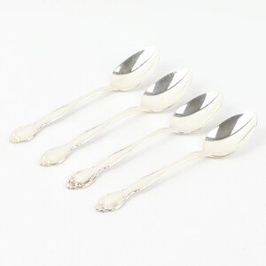 May include: Four silver teaspoons with ornate handles. The spoons are arranged in a row, with the handles pointing to the right.