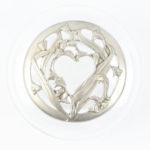 May include: A silver-toned metal lid with a heart-shaped cutout surrounded by a floral design.
