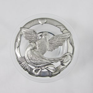 May include: A silver-toned glass jar lid with a decorative design of two doves intertwined with a heart. The doves are in a circular frame with a ribbon design.