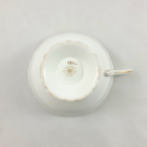 May include: White porcelain teacup with a gold rim and a gold Coalport logo on the bottom. The logo includes a crown and the text "Coalport Fine China England Est. 1750".