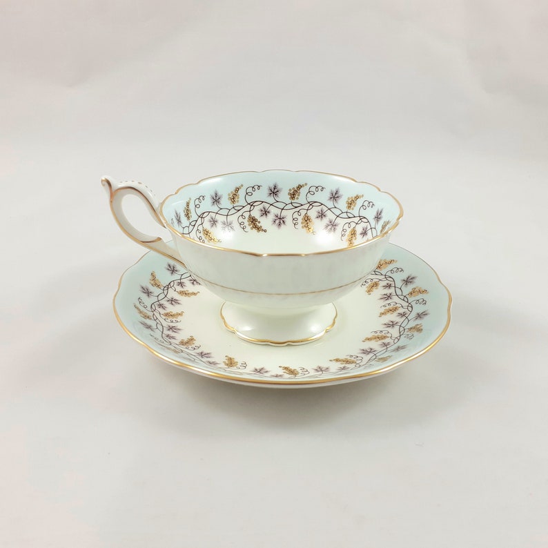 May include: A delicate teacup and saucer set with a pale blue background and a gold and purple floral design.