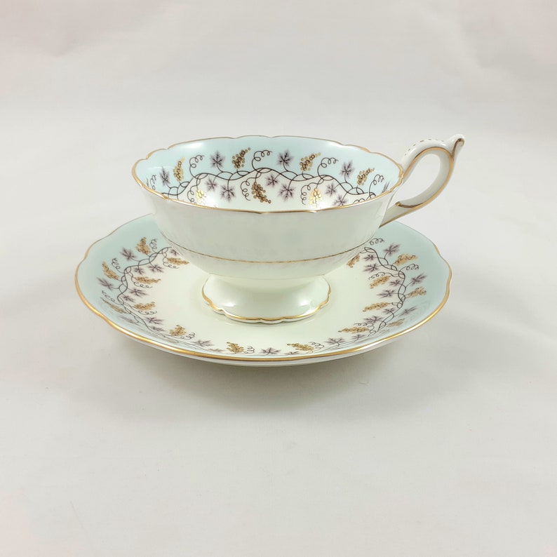 May include: A delicate teacup and saucer set with a pale blue background and a gold and purple floral design.