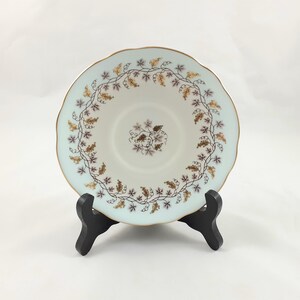 May include: A white porcelain saucer with a delicate blue and gold floral design. The saucer features a vine pattern with small purple and gold flowers.