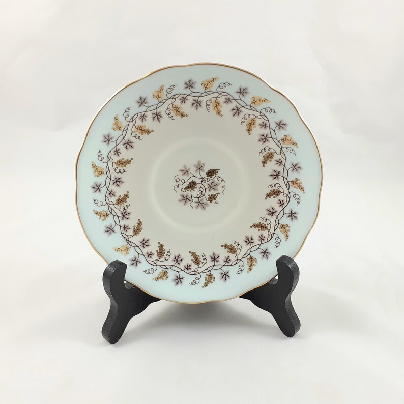 May include: A white porcelain saucer with a delicate blue and gold floral design. The saucer features a vine pattern with small purple and gold flowers.