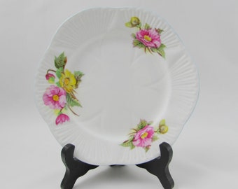 May include: A white porcelain plate with a scalloped edge and a blue trim. The plate features a floral design with pink and yellow flowers.