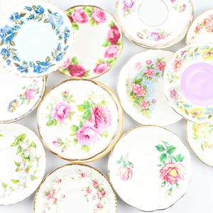 May include: A collection of ten vintage teacups and saucers featuring floral patterns in shades of pink, blue, and yellow. The saucers have gold trim.