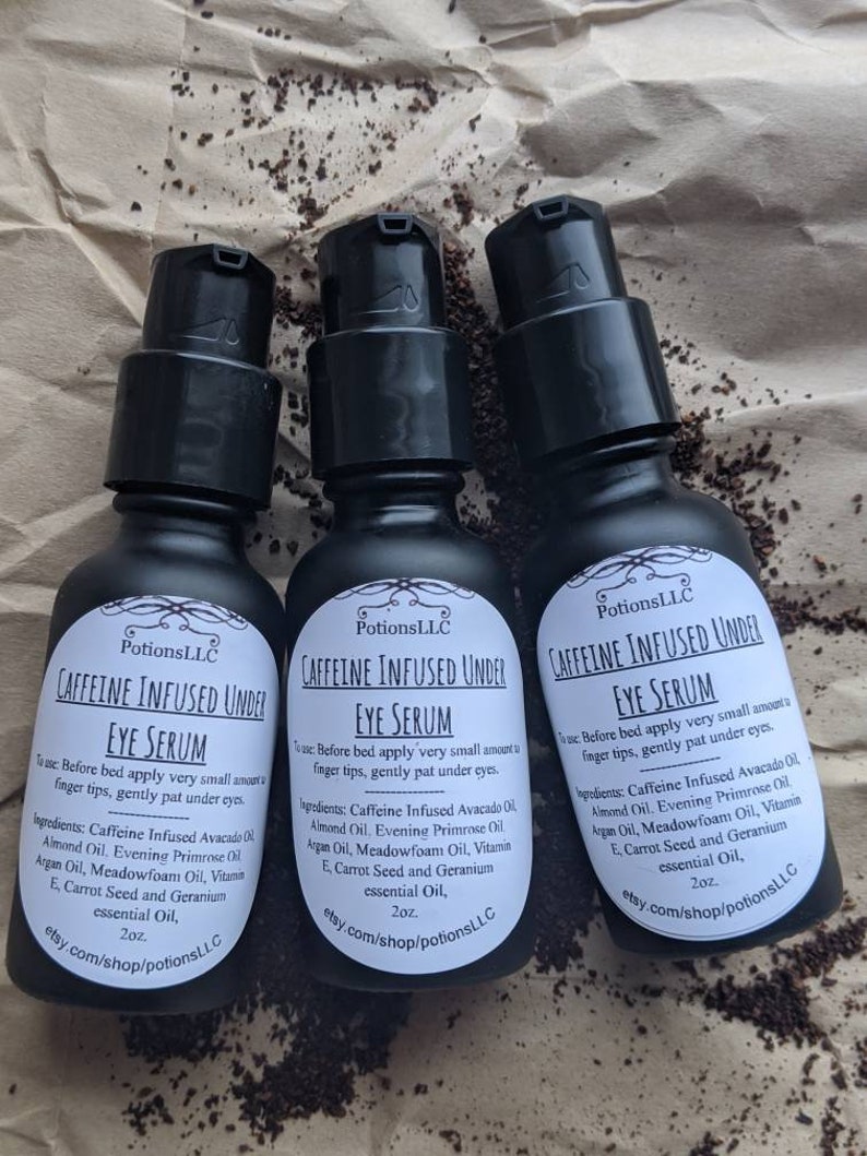 May include: Three 2 ounce bottles of caffeine infused under eye serum. The bottles are black with white labels and the text "Caffeine Infused Under Eye Serum" is printed on the front of each bottle. The ingredients are listed on the label: Caffeine Infused Avocado Oil, Almond Oil, Evening Primrose Oil, Argan Oil, Meadowfoam Oil, Vitamin E, Carrot Seed and Geranium essential Oil. The bottles are sitting on a brown surface.