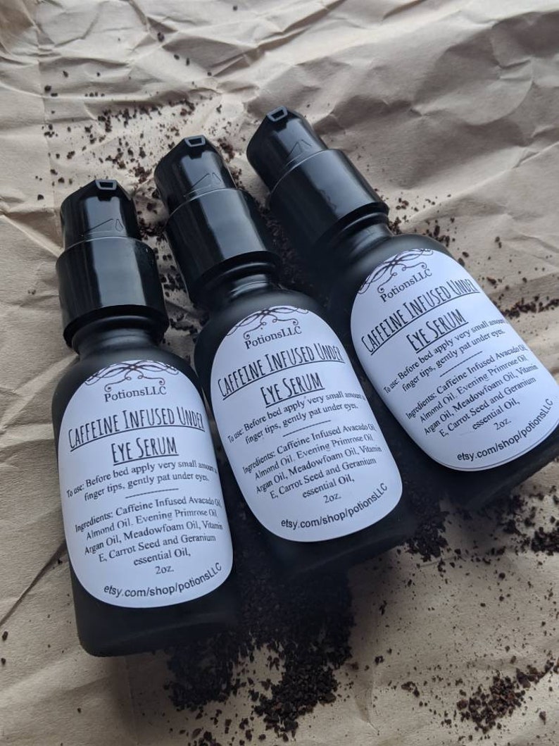 May include: Three 2 ounce bottles of Caffeine Infused Under Eye Serum. The bottles are black with white labels and the text "Caffeine Infused Under Eye Serum" is printed on the labels. The bottles are sitting on a brown paper surface.