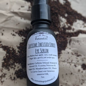 May include: A black glass bottle with a white label that reads "Caffeine Infused Under Eye Serum" and lists the ingredients. The bottle is sitting on a brown surface with coffee grounds scattered around it.