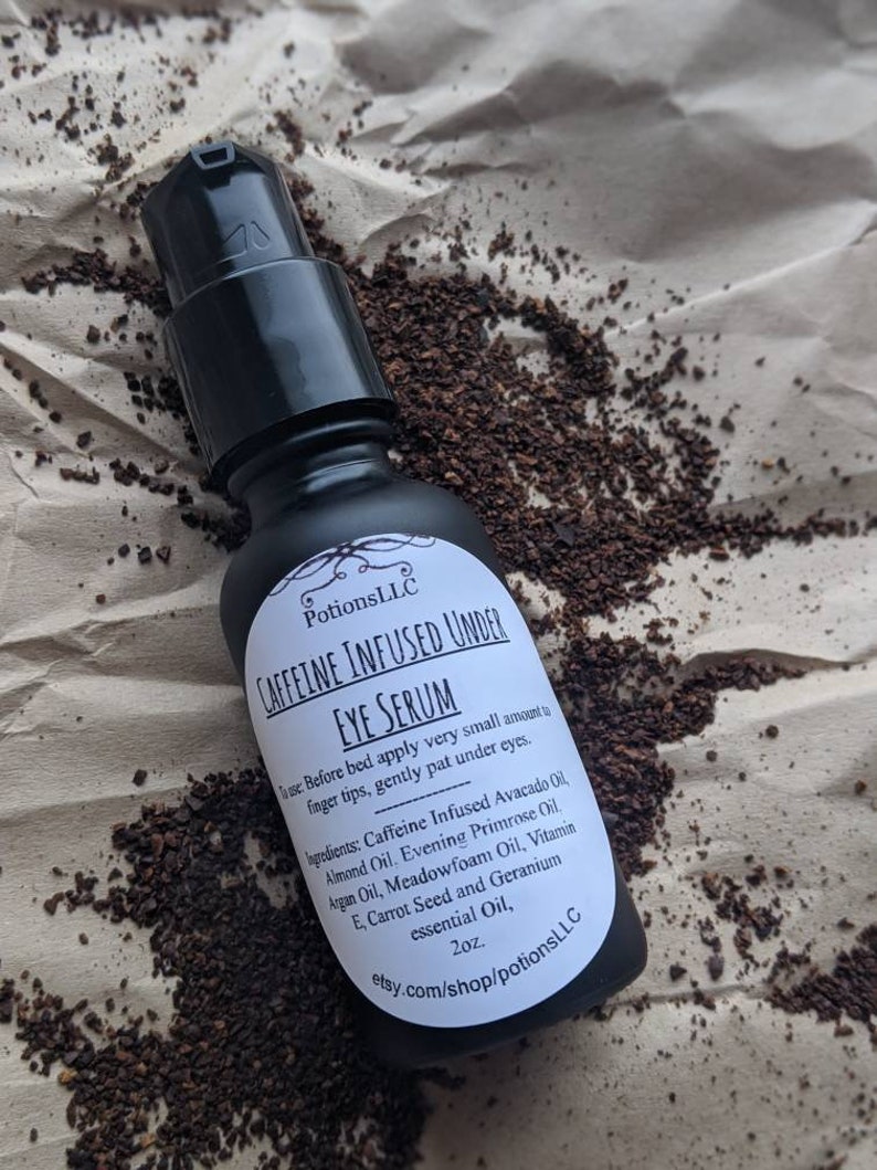 May include: A black bottle with a white label that reads "Caffeine Infused Under Eye Serum" and lists the ingredients. The bottle is sitting on a brown surface with coffee grounds.