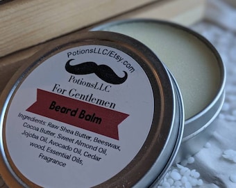 Può includere: Una scatola di latta argentata con un'etichetta bianca che recita "Potions LLC/Etsy.com", "Potions LLC", "For Gentlemen", "Beard Balm", e elenca gli ingredienti. La scatola è aperta e il balsamo è visibile all'interno.