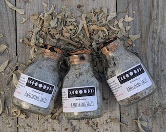 May include: Three small glass bottles with cork tops filled with gray salt crystals. Each bottle has a white label with black text that reads "Potions LLC Banishing Salts" and a black and white moon phase graphic.