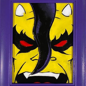 May include: A framed painting of a yellow monster with black hair and red eyes. The monster has a menacing expression and sharp teeth.