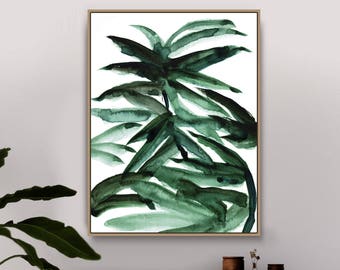 May include: A watercolor painting of a green tropical plant with a white background. The painting is framed in a light wood frame and is hanging on a white wall above a wooden cabinet.