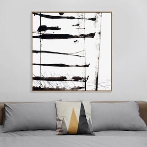 May include: Abstract black and white artwork in a gold frame. The painting features bold, horizontal brushstrokes and splatters. The artwork hangs above a bed with grey pillows and a decorative pillow with geometric shapes.