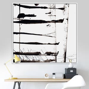 May include: Abstract black and white artwork in a white frame. The painting features horizontal and vertical black brushstrokes and splatters on a white background. The artwork is displayed above a wooden desk with a yellow lamp.
