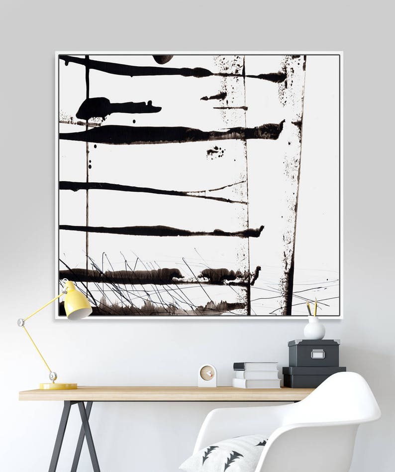 May include: Abstract black and white artwork in a white frame. The painting features horizontal and vertical black brushstrokes and splatters on a white background. The artwork is displayed above a wooden desk with a yellow lamp.