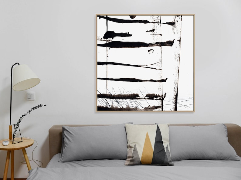 May include: Abstract black and white artwork in a gold frame. The painting features bold, horizontal brushstrokes and splatters. The artwork hangs above a bed with grey pillows and a decorative pillow with geometric shapes.