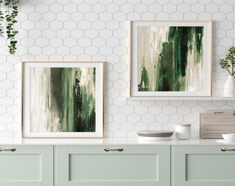 May include: Two framed abstract paintings with green and white brushstrokes on a white tiled wall above a kitchen counter with green cabinets.