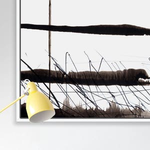 May include: Abstract black and white artwork in a white frame. The painting features bold black brushstrokes and lines against a white background. A yellow desk lamp with a white interior is in the lower left corner.