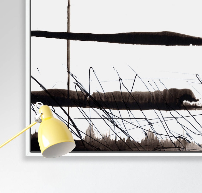 May include: Abstract black and white artwork in a white frame. The painting features bold black brushstrokes and lines against a white background. A yellow desk lamp with a white interior is in the lower left corner.
