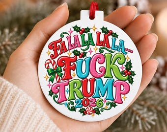 Puede incluir: Un adorno navideño redondo de cerámica blanca con texto colorido que dice "FA LA LA LA LA... FUCK TRUMP 2026". El diseño incluye hojas de acebo rojas y verdes, bayas, un bastón de caramelo y pequeñas estrellas amarillas sobre un fondo blanco.