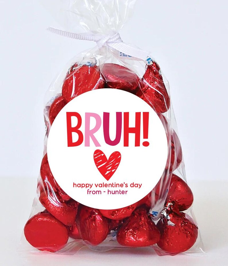 May include: A white circle sticker with red and pink text that says "BRUH!" with a red heart and the text "happy valentine's day from - hunter". The sticker is on a clear plastic bag filled with red foil-wrapped chocolate kisses.