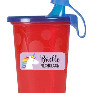 May include: Red plastic cup with a blue lid and handle. The cup has a purple label with a unicorn and rainbow design. The label says "Brielle Nicholson".
