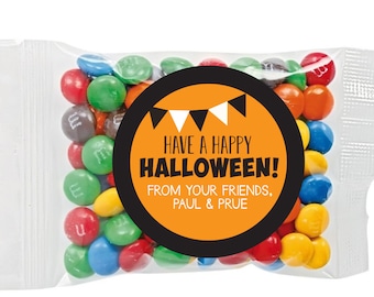 Könnte beinhalten: Ein kleiner transparenter Plastikbeutel gefüllt mit bunten M&M's-Bonbons. Ein runder Aufkleber mit schwarzen und orangen Rändern und weißem Text lautet "Have a Happy Halloween! From your friends, Paul & Prue."
